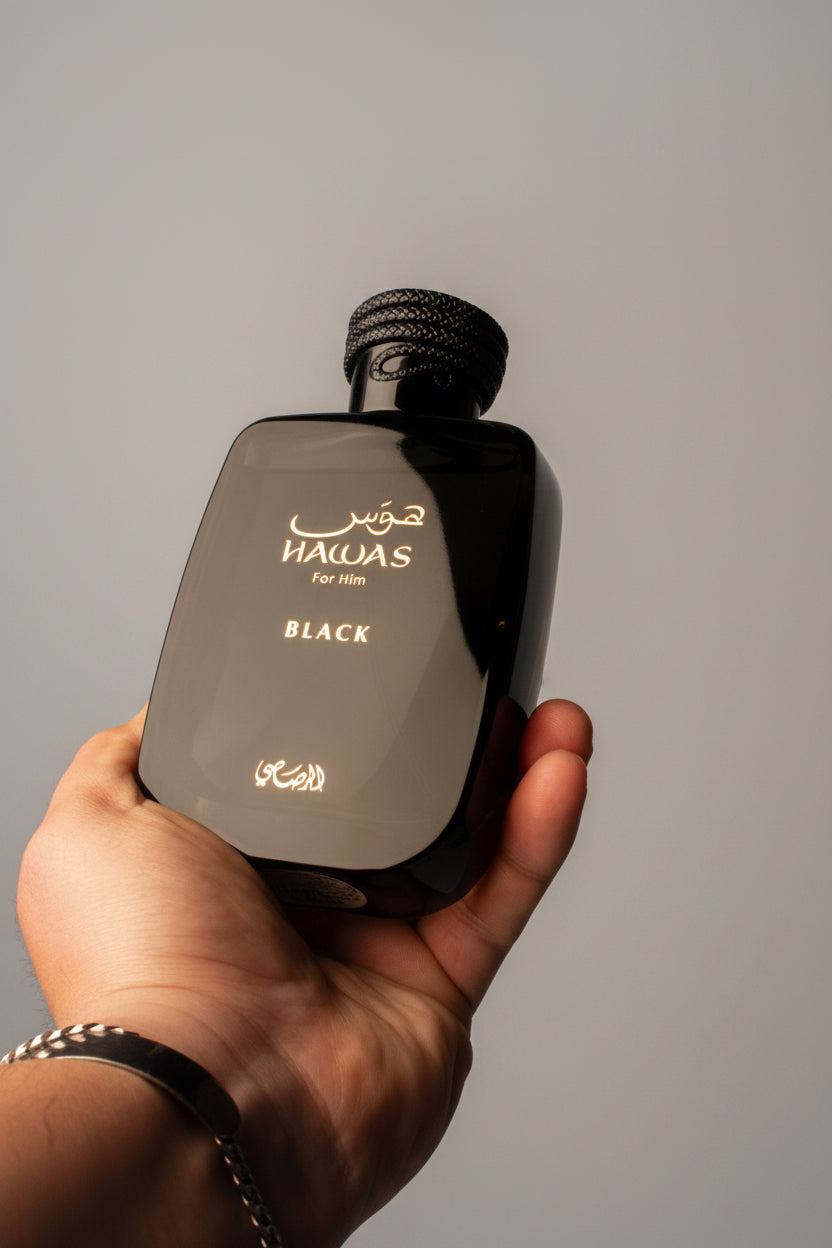 Hand holding a Halyas for Him Black perfume bottle against a dark background