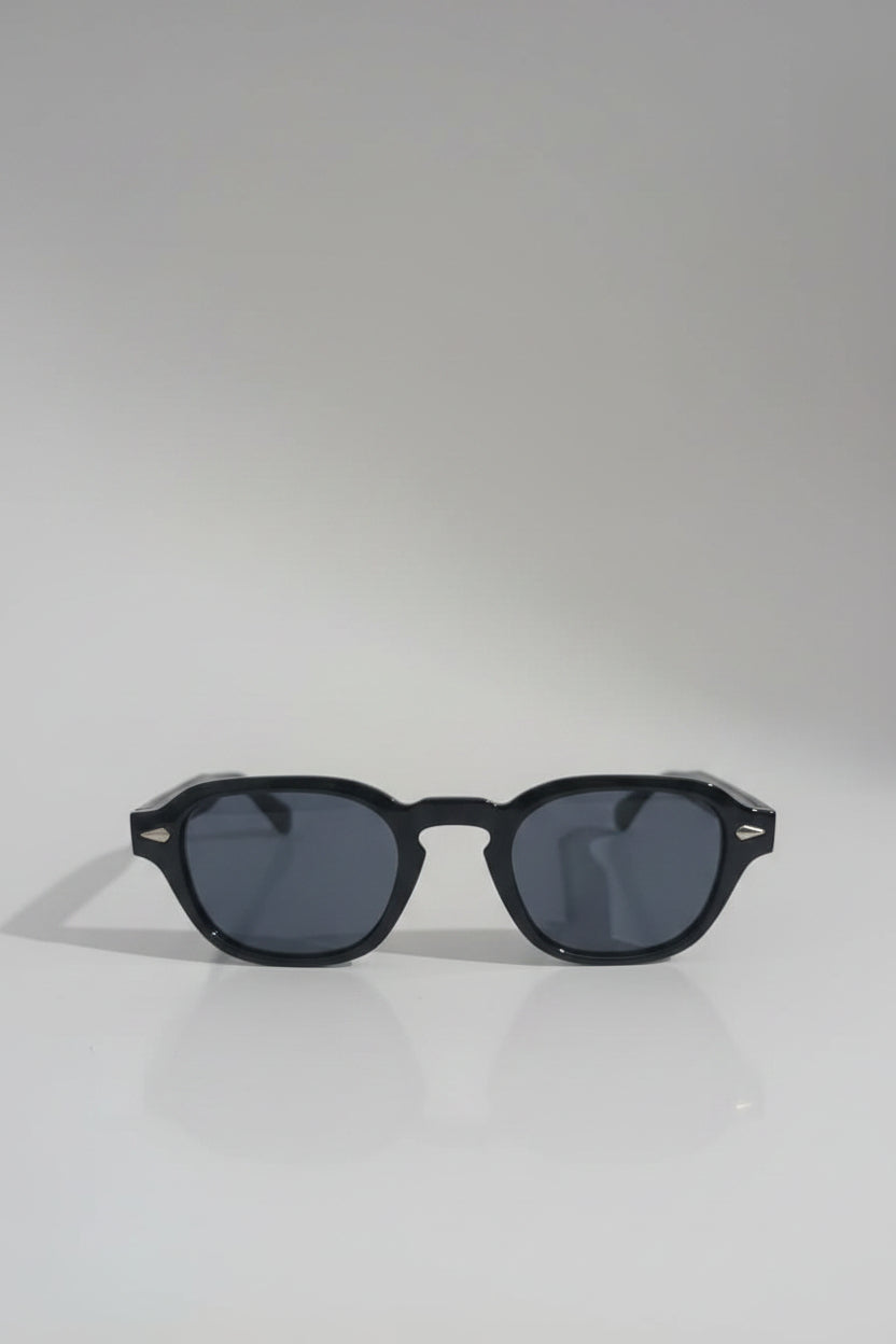 Black sunglasses with dark lenses on a white surface, with a blurred red patterned fabric in the background.