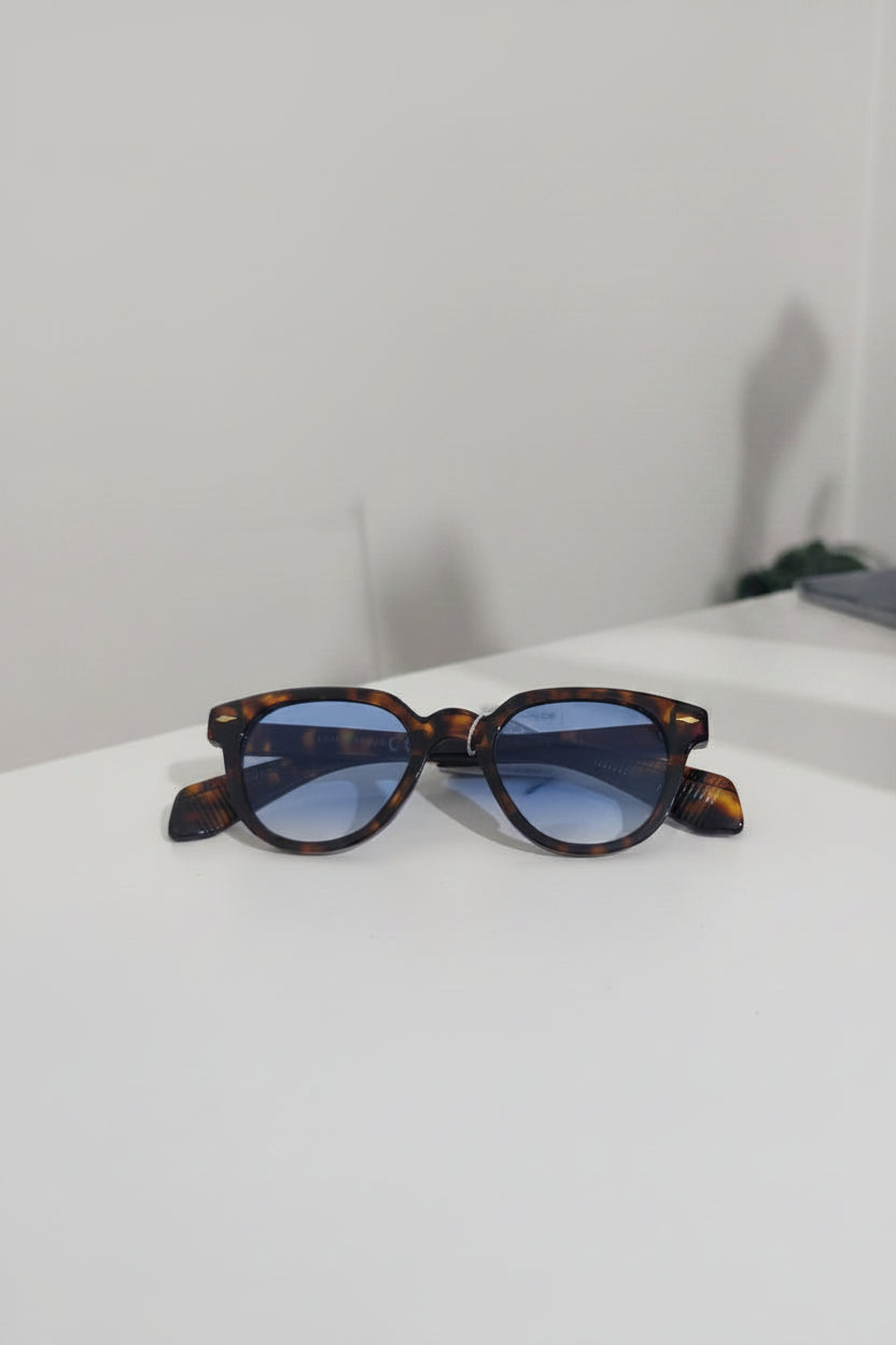Sunglasses with tortoiseshell frame and blue lenses on a white surface